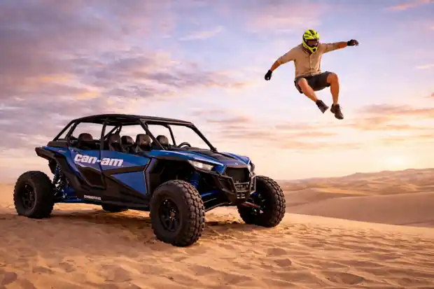 Adventure rider jumping in air beside blue Can-Am dune buggy at sunset desert