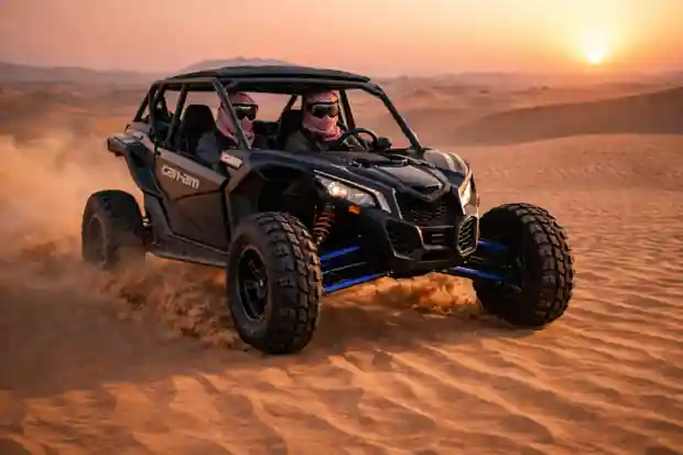 Two riders driving a dune buggy across desert sand at sunset with warm golden light