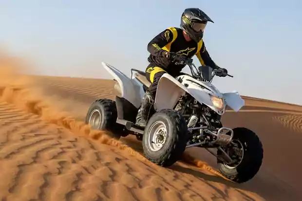 Grizzly - White quad bike riding in desert dunes with rider wearing helmet, real off-road adventure