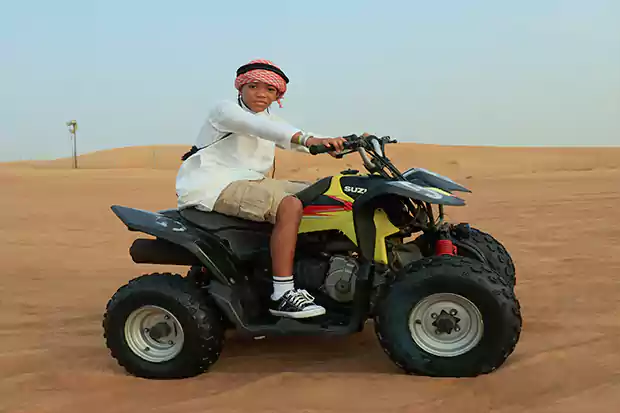 Kid riding quad bike in desert with safety gear during guided desert adventure